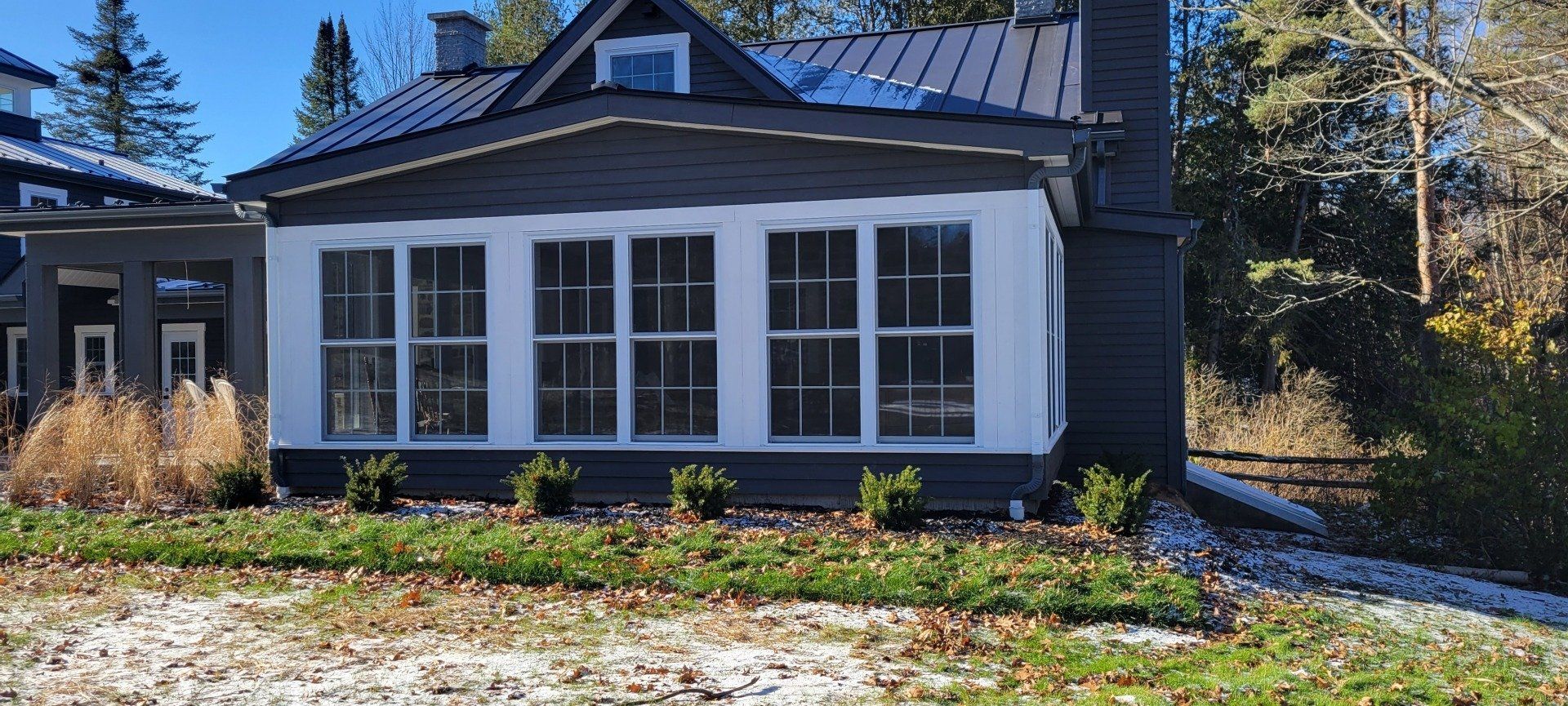 Une maison noire et blanche avec beaucoup de fenêtres est située au sommet d'une colline verdoyante.