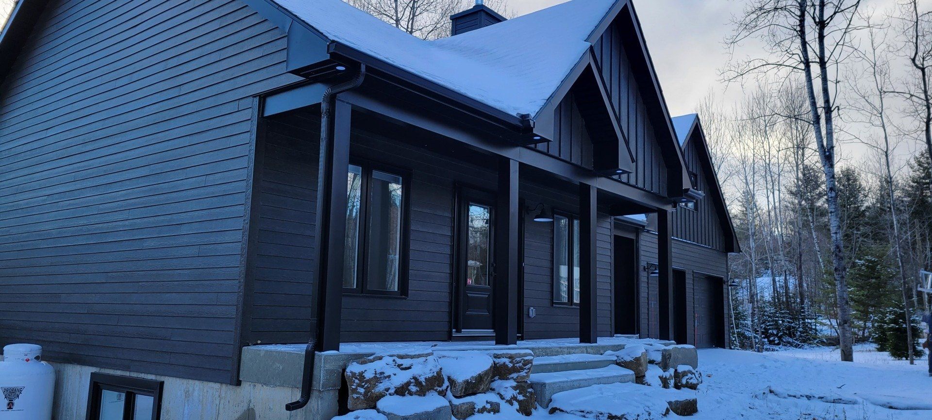 Une maison noire avec un porche et des escaliers dans la neige.