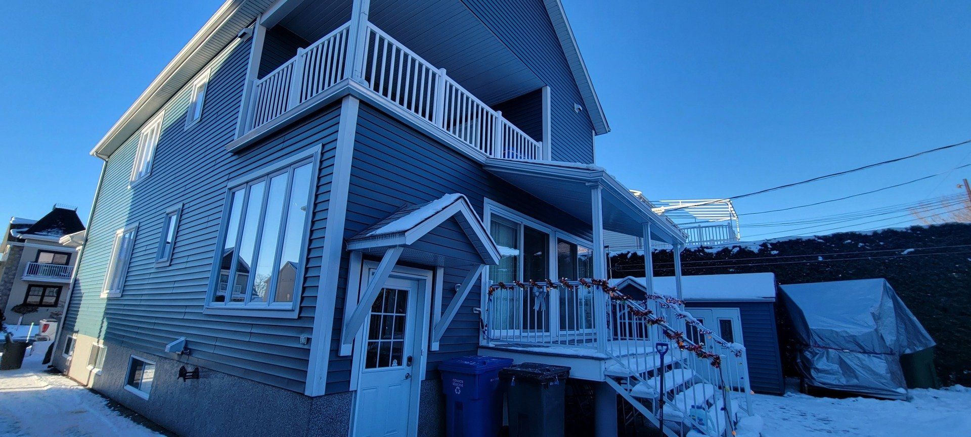 Une grande maison avec un balcon et beaucoup de fenêtres est recouverte de neige.