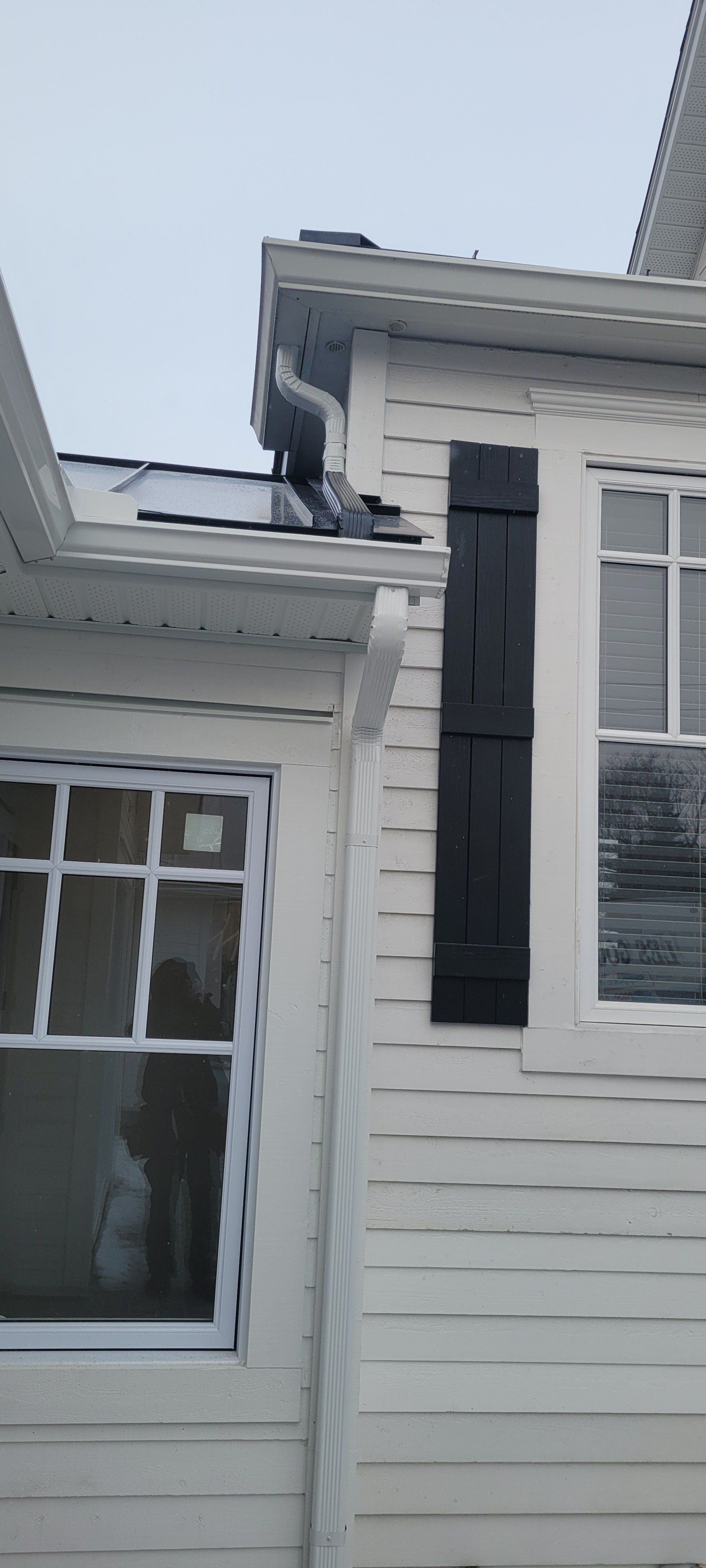 Une maison blanche avec des volets noirs aux fenêtres et un oiseau sur le toit.