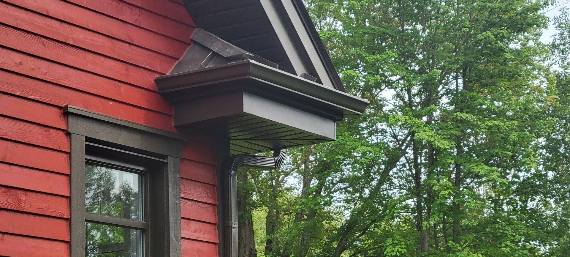 Une maison rouge avec une fenêtre et un porche entouré d'arbres.