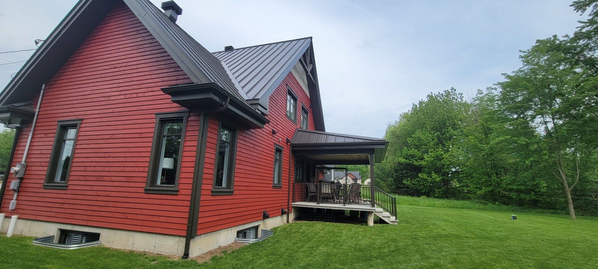 Une maison rouge avec un toit noir se trouve au milieu d'un champ vert luxuriant.