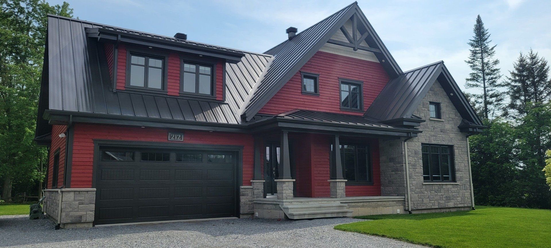 Une grande maison rouge avec une porte de garage noire est située au sommet d'une colline verdoyante.