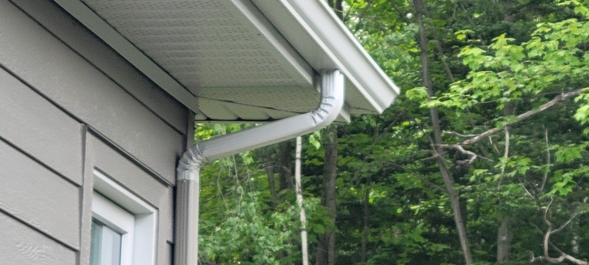 Une gouttière blanche est fixée sur le côté d'une maison.