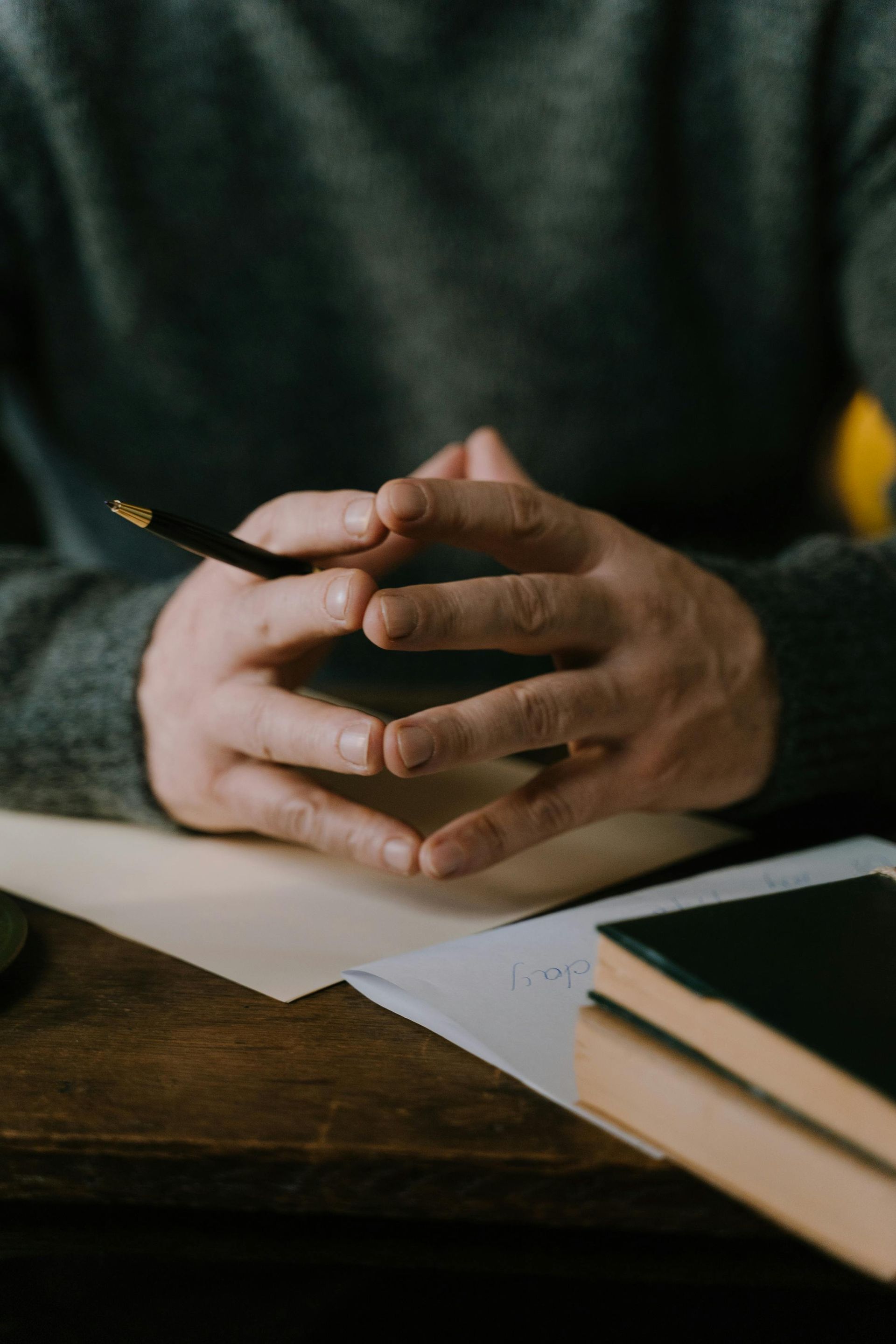 A man is sitting at a table with his hands folded and holding a pencil.