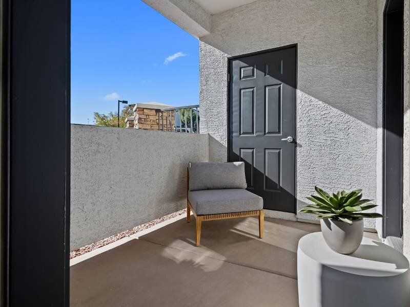 Private apartment balcony with a gray cushioned chair and a potted succulent by a dark door.
