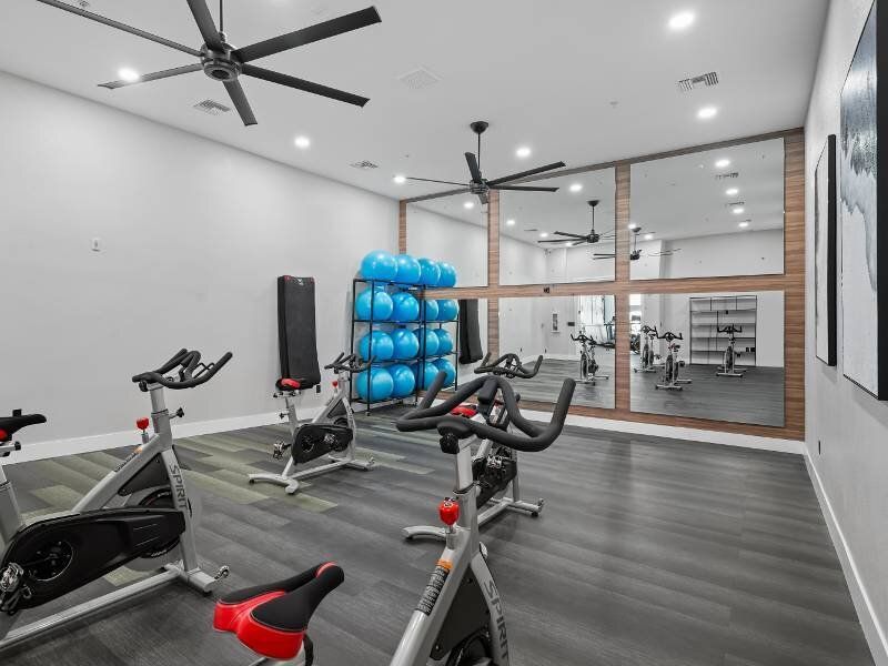 Interior of a resident gym with cardio bikes, blue exercise balls, and a mirrored wall.