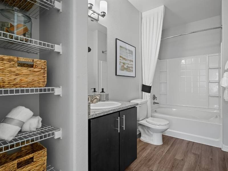 Bathroom inside a modern apartment with a dark vanity, granite countertop, toilet, and a tub/shower.