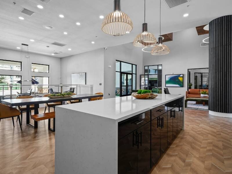 Modern communal lounge with a large white kitchen island, pendant lights, and seating areas.