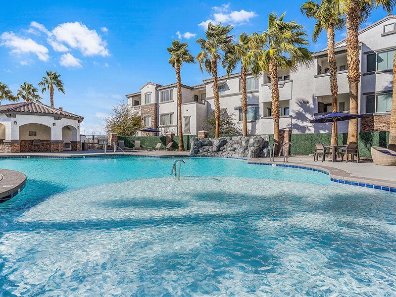 Outdoor resort-style pool with palm trees and lounge seating at an apartment community.