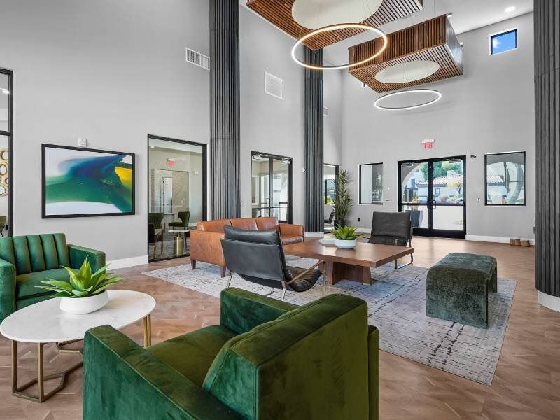 Modern apartment community lobby with green sofas, a wooden coffee table, and circular pendant lights.