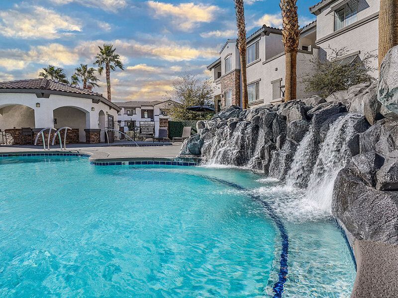 Outdoor pool with a cascading rock waterfall at an apartment community.