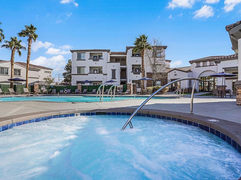 Outdoor community pool area with lounge chairs and apartment buildings in the background.