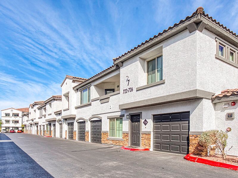 Exterior view of a row of townhouse-style apartment buildings with attached garages and a blue sky.