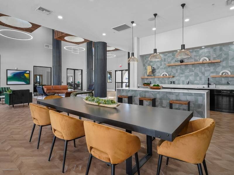 Modern communal lounge with a large dining table, mustard chairs, and a sleek kitchen.