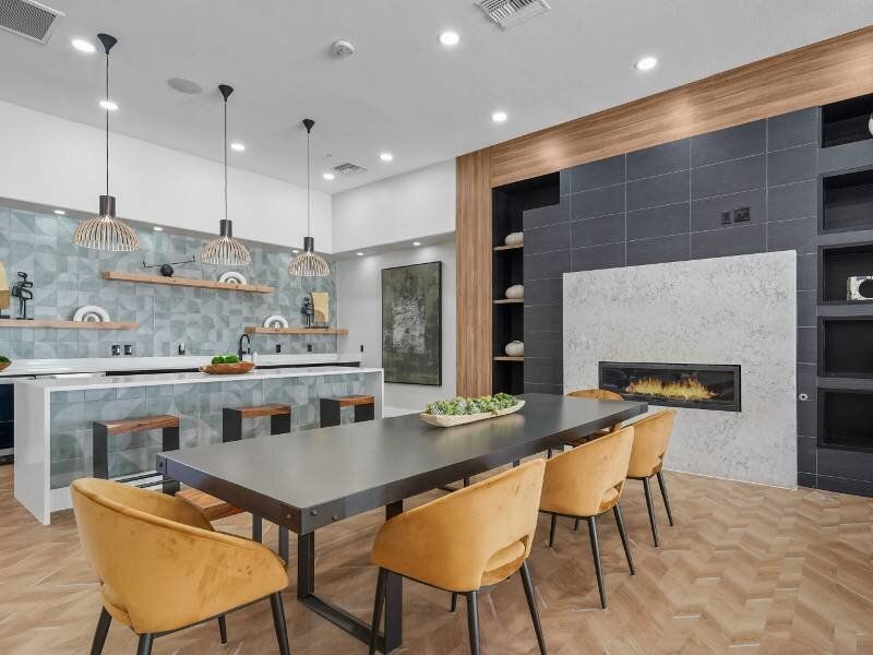 Modern resident amenity lounge with a kitchen island, long dining table, and fireplace.