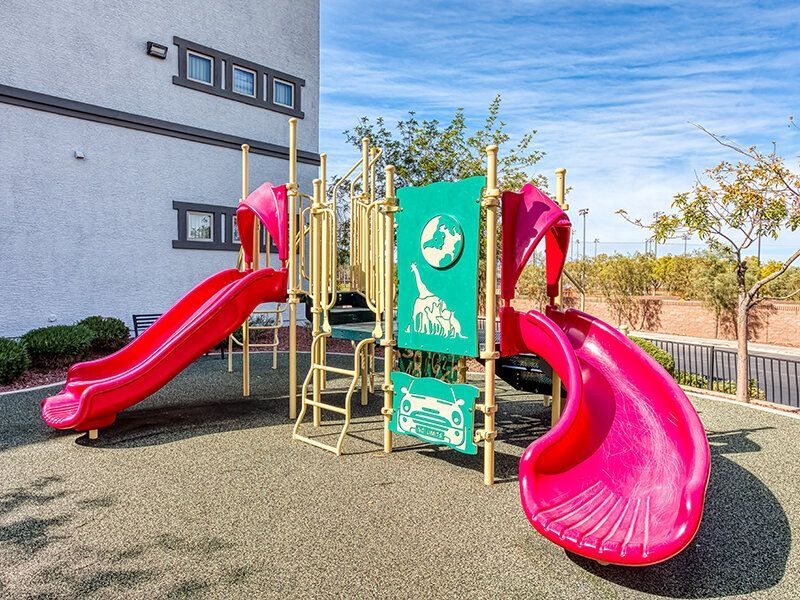 Colorful playground with red slides beside a gray apartment building.