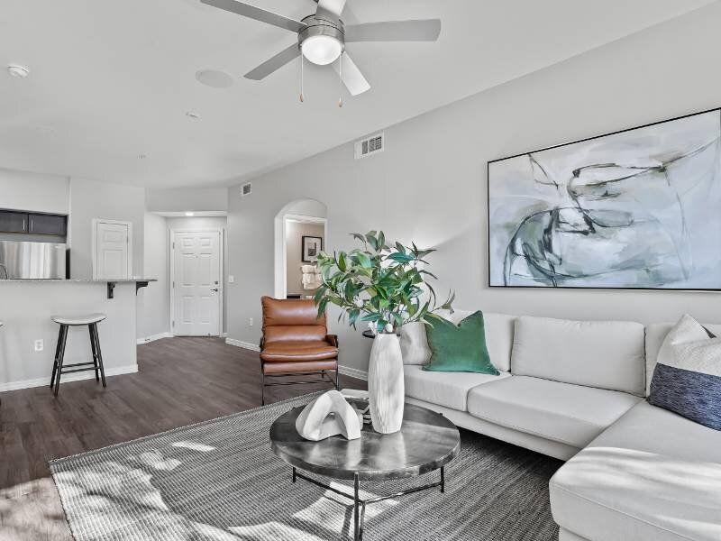 Modern apartment living room with white sectional, abstract art, plant, and open kitchen.