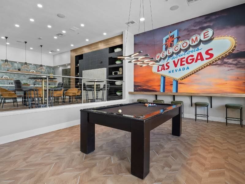 Interior community recreation room with a pool table, seating area, and a Las Vegas mural.