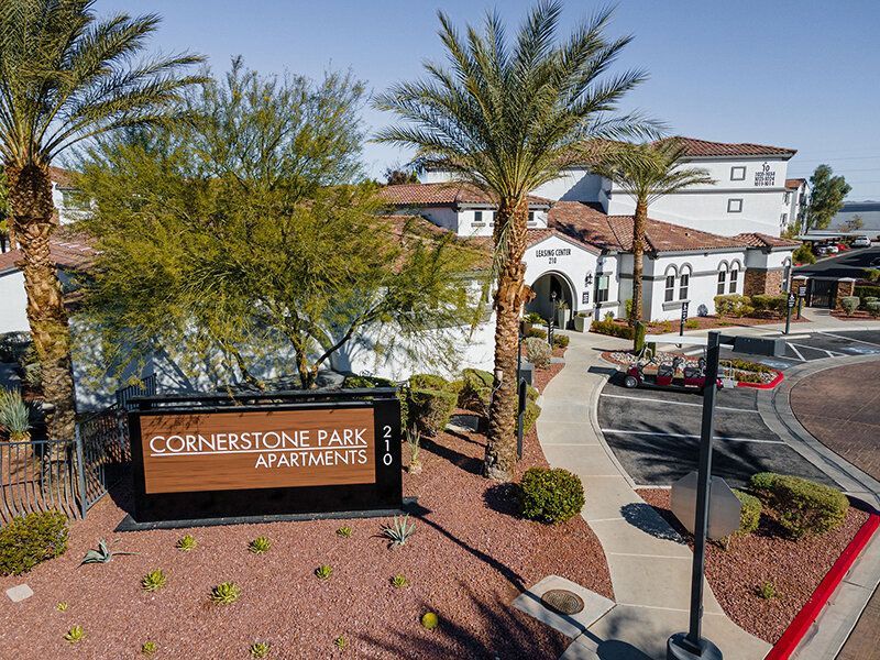Aerial view of Cornerstone Park Apartments entrance with sign, drive, and palm trees.