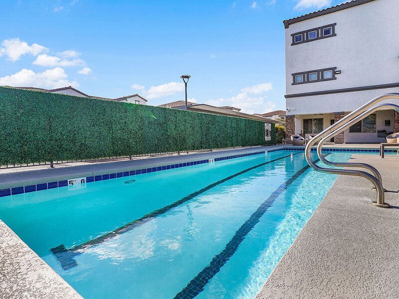 Outdoor rectangular pool at apartment complex with a green hedge, white building, and stainless handrail.