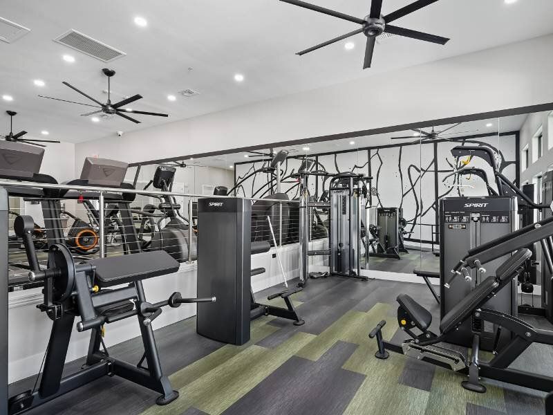 Interior view of a modern apartment fitness center with treadmills, weight machines, and mirrors.