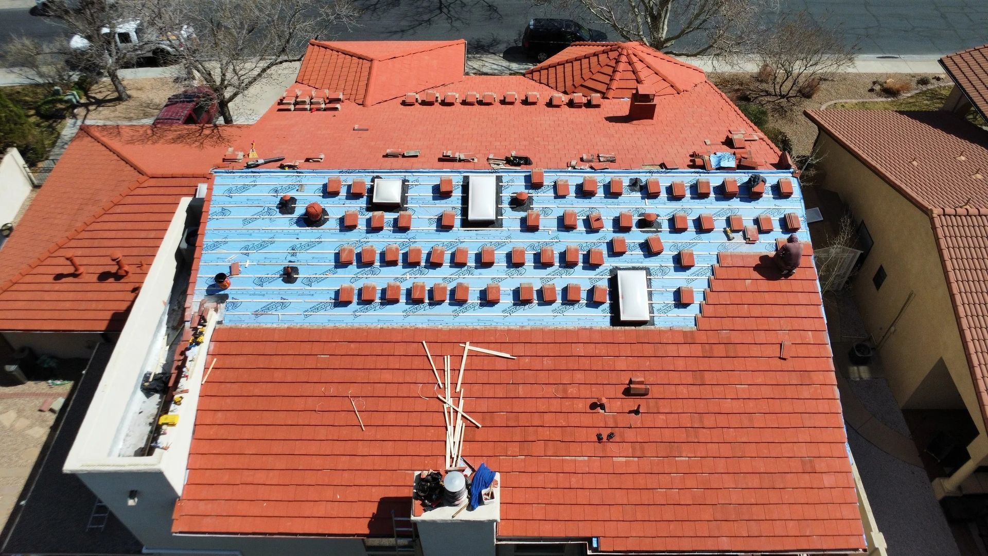 Aerial view of a home with a red tile roof under renovation. Some tiles are removed, revealing blue underlayment.