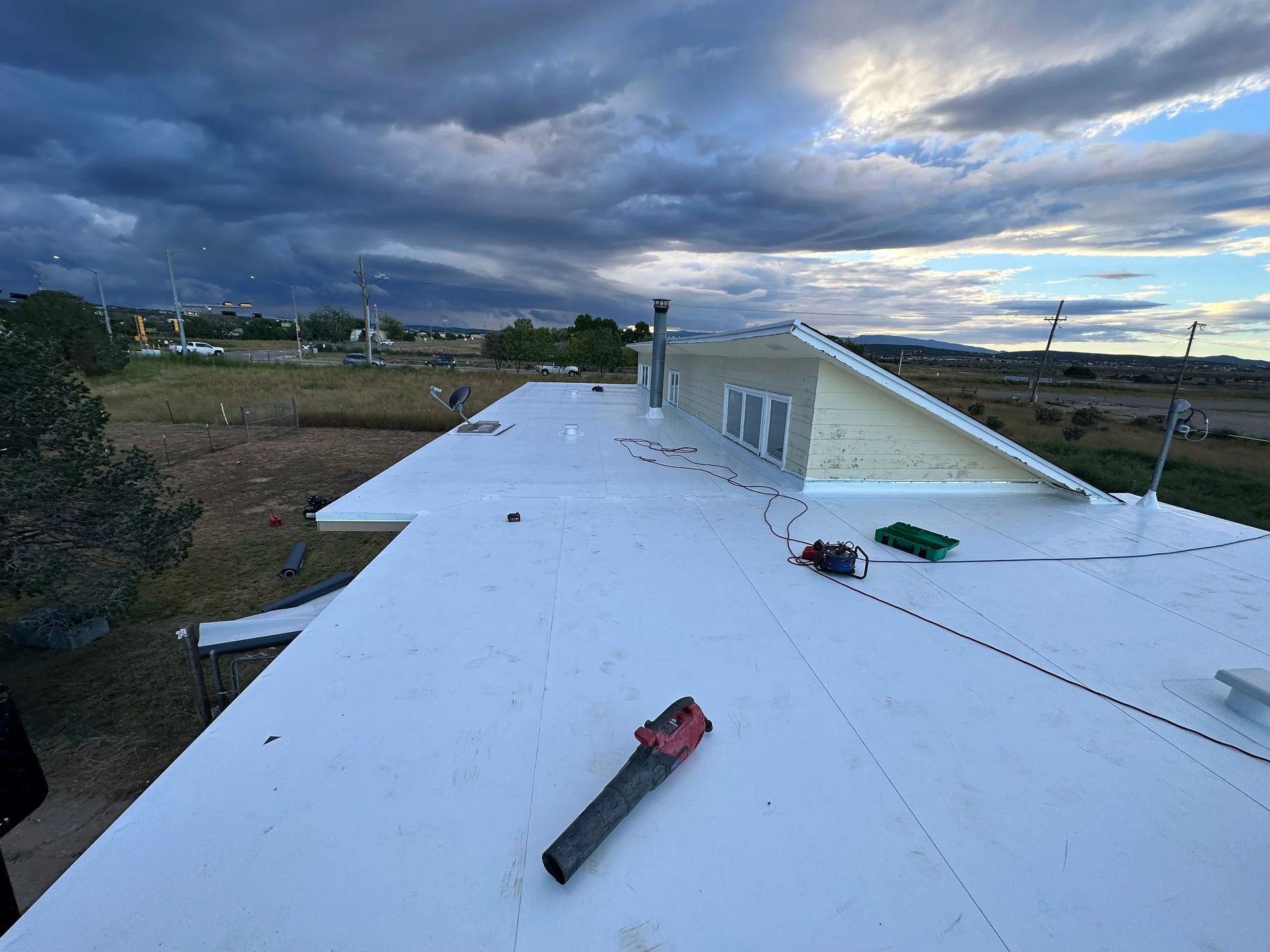 Overhead view of a flat, white roof with tools, against a cloudy sky and distant landscape.