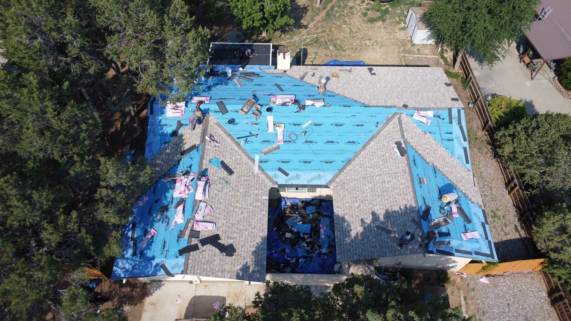 Aerial view of a house roof under construction, blue tarp covering sections.