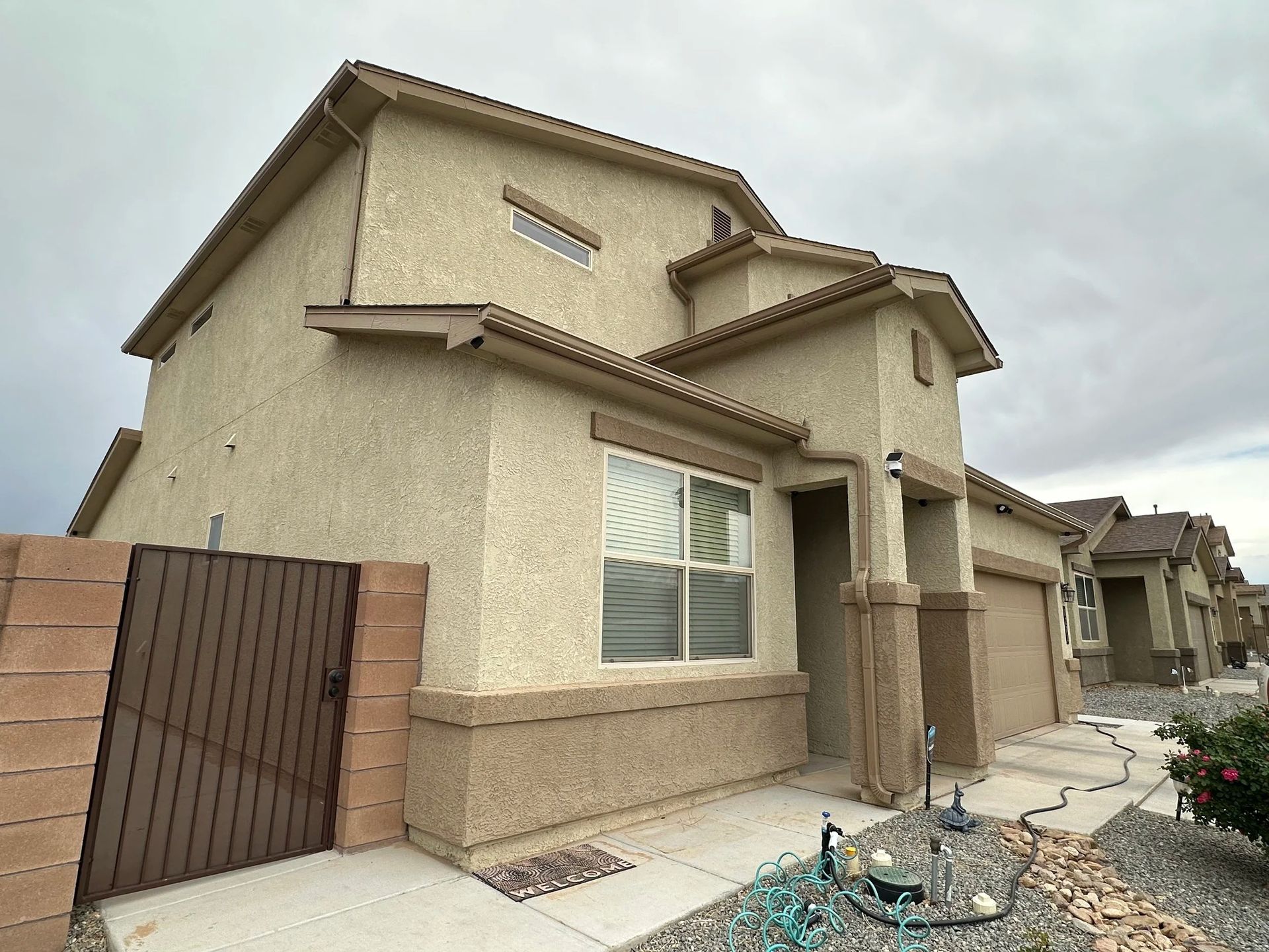 Two-story stucco house with a brown gate, beige siding, and cloudy sky.
