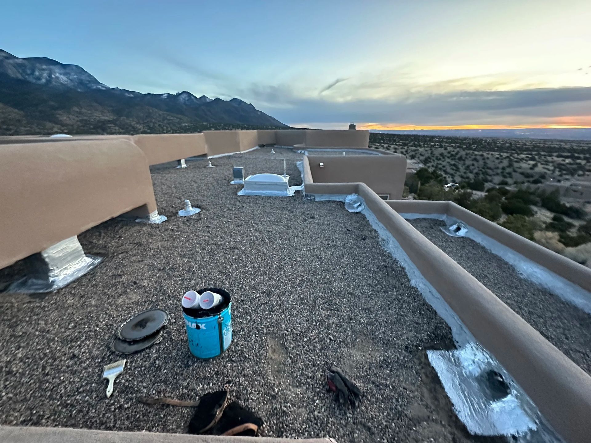 Rooftop with gravel surface and low walls against a desert landscape, bucket, tools present.