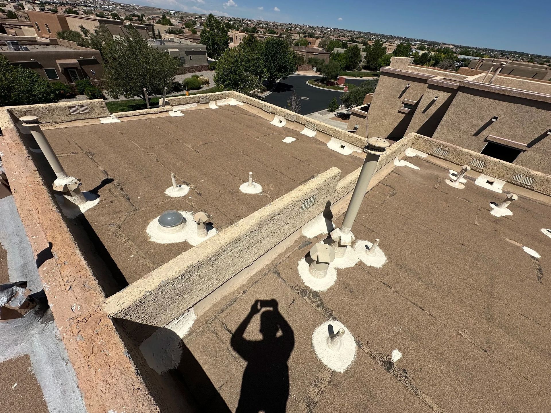 A rooftop with various vents, a domed skylight, and a person's shadow holding a phone.