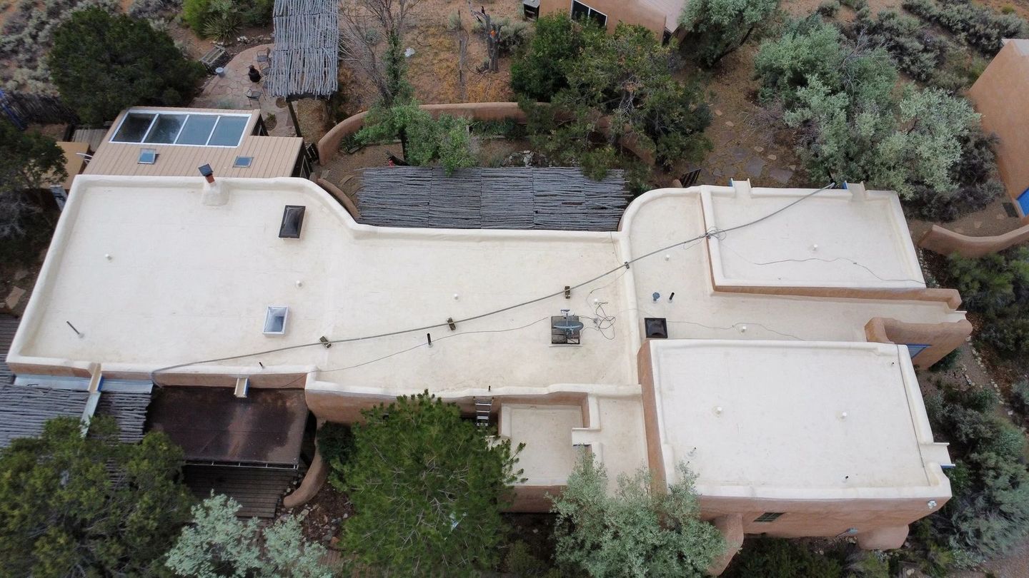 Overhead view of a light beige adobe-style building with a flat roof, string lights, and surrounding greenery.