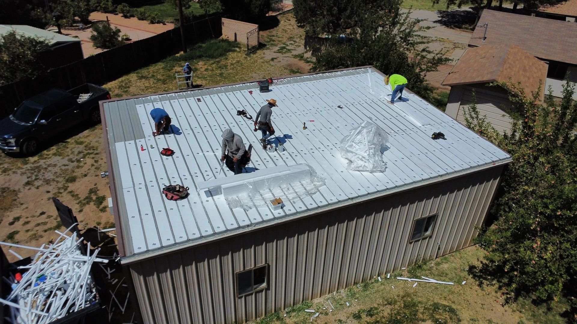 Roofers installing metal roofing on a small, wood-sided building; aerial view.