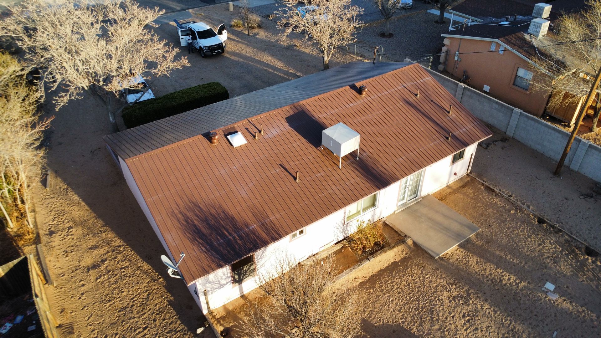 Workers installing a metal roof on a small building. Bright sunlight, outdoor setting.