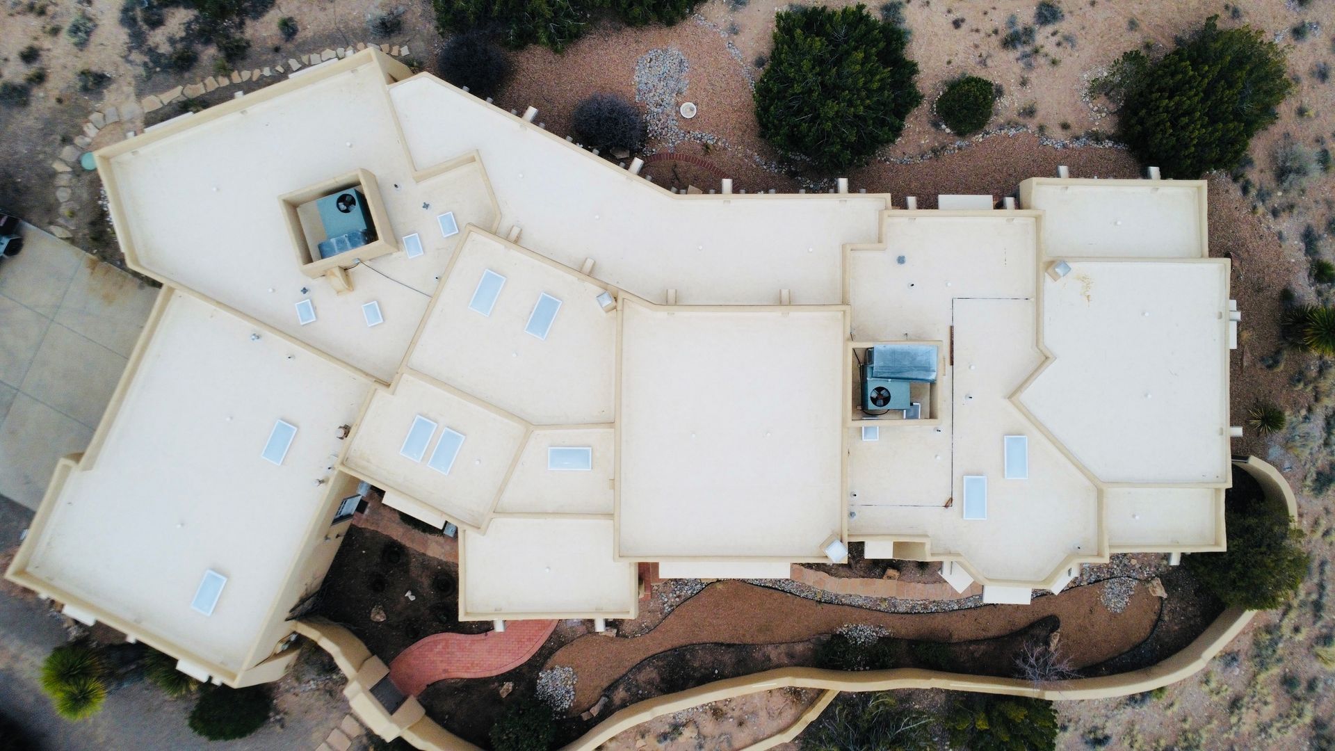 Overhead view of a large, light-colored house with a complex roof structure and skylights on a hillside.