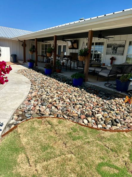 Stone path along a house's covered porch with blue flower pots, green grass, and a clear blue sky.