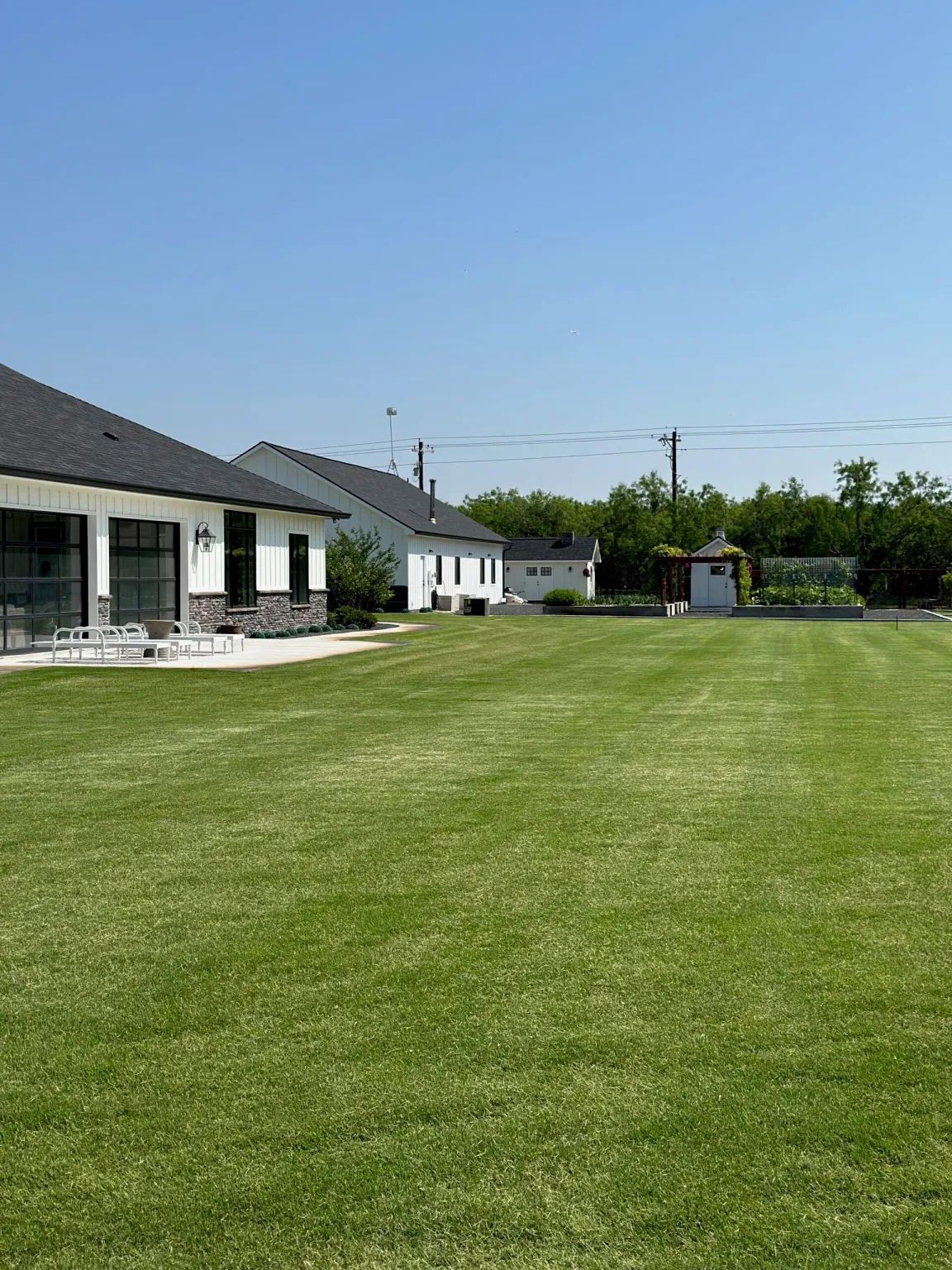 Lush green lawn with several white houses and a garden under a clear blue sky.