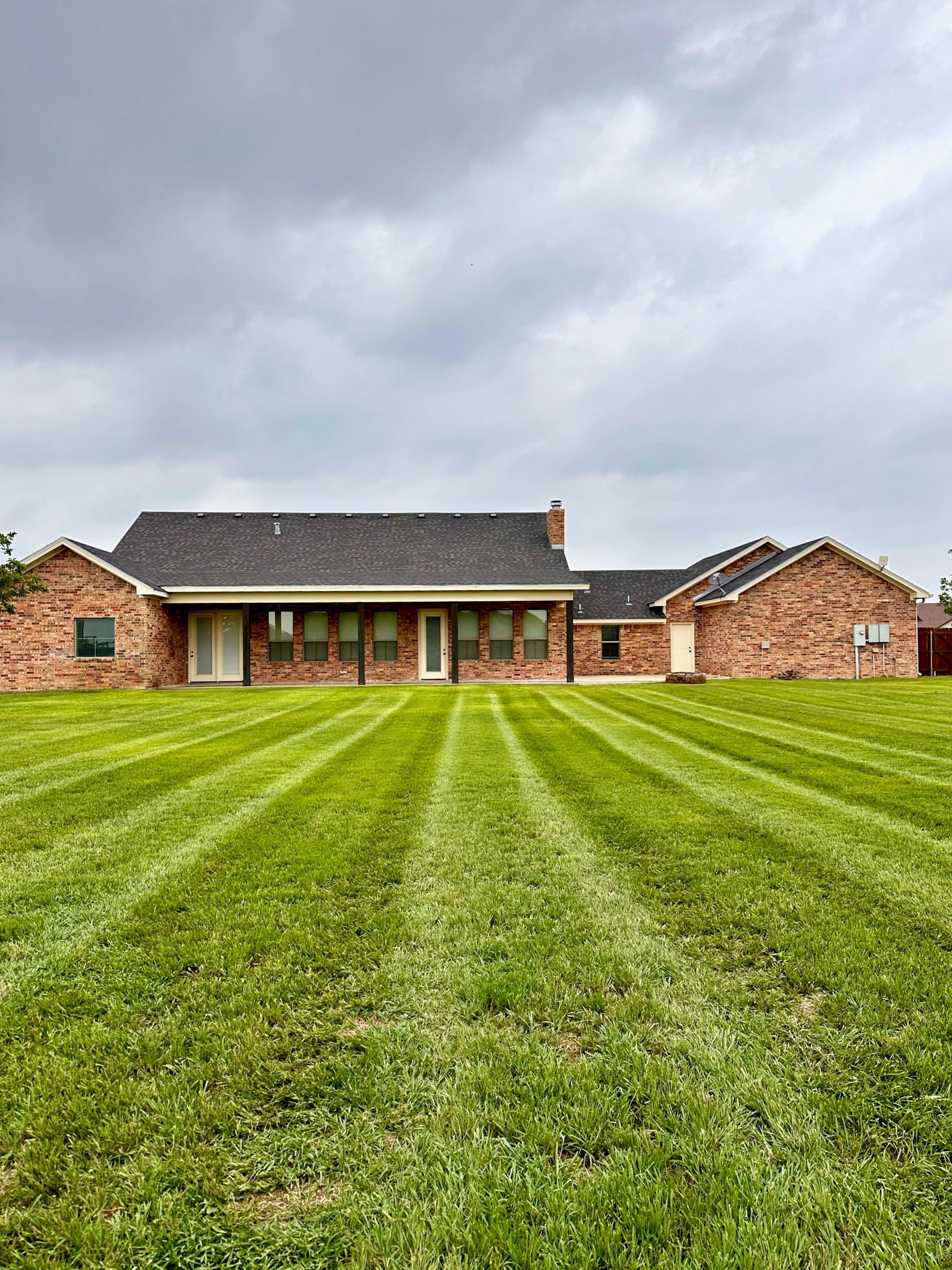 Green lawn striped from mowing in front of a brick house on a cloudy day.