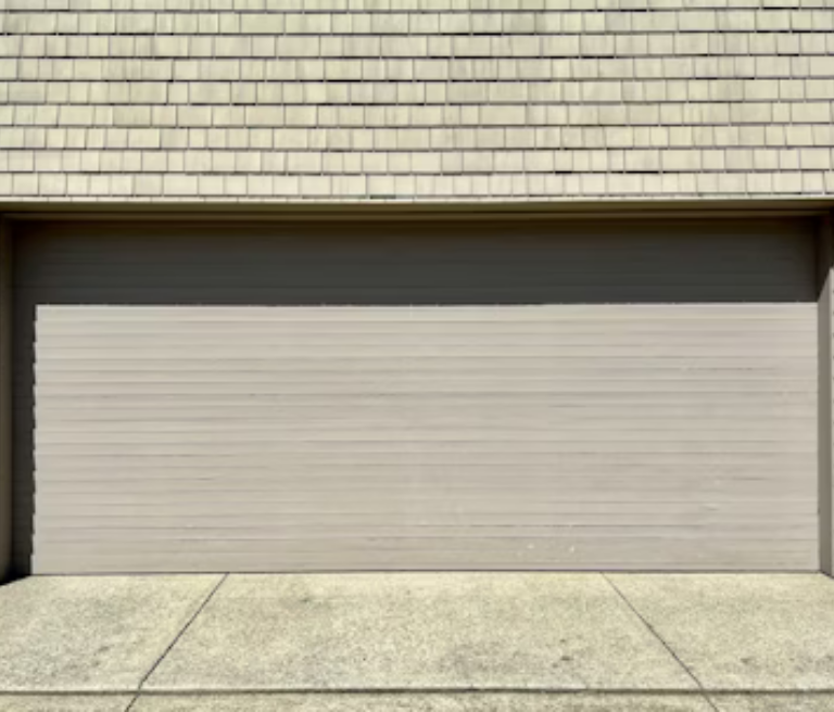 Beige garage door under a light brown shingled roof, set against a concrete driveway.