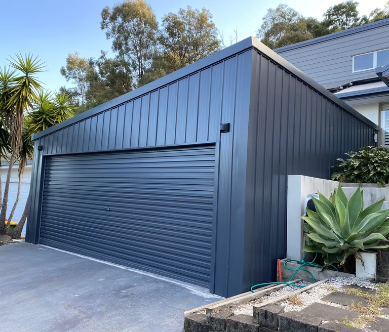 Dark gray garage with a roll-up door, next to a house with a gray tile roof.