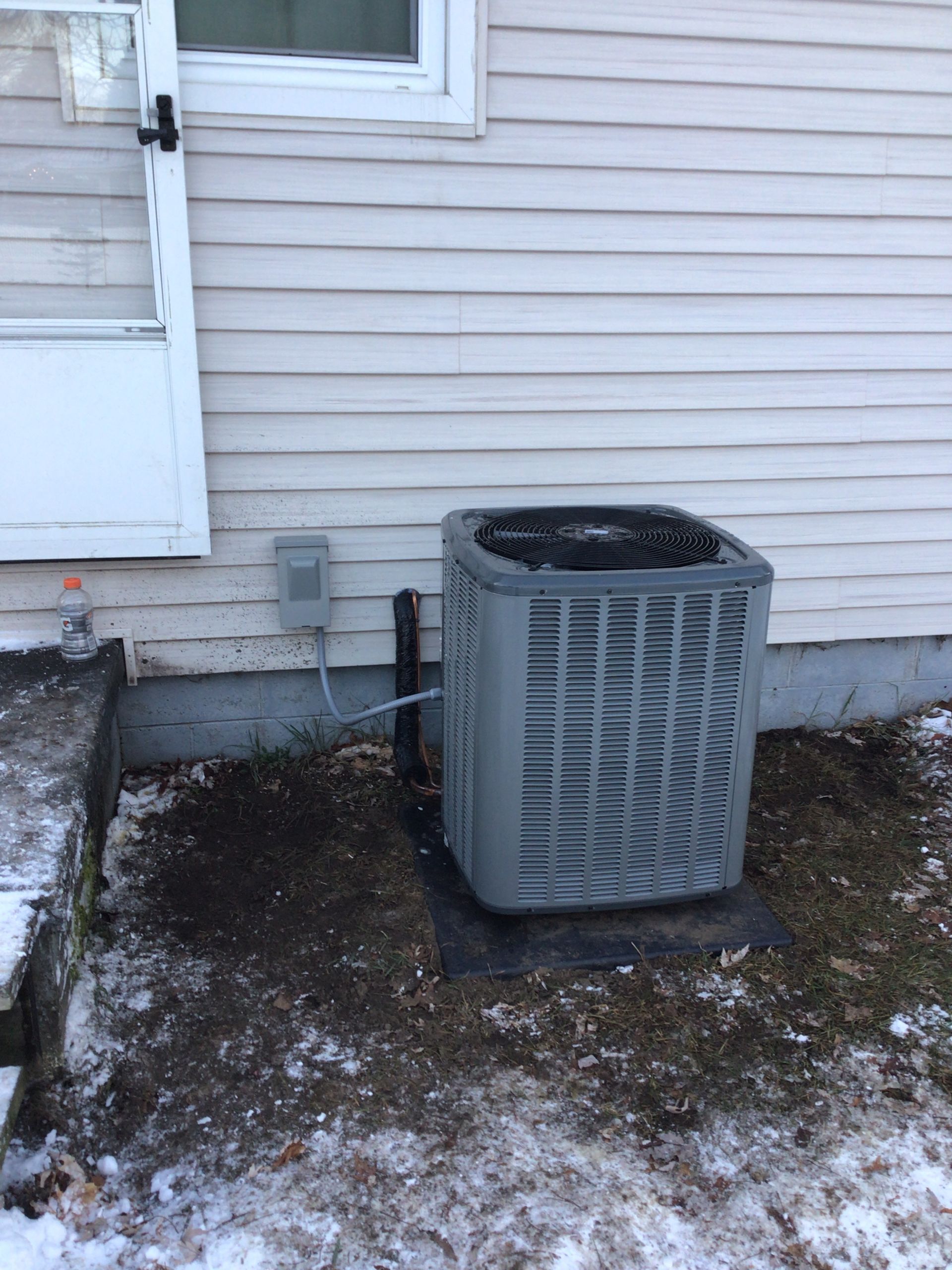 An air conditioner is sitting on the side of a house in the snow.