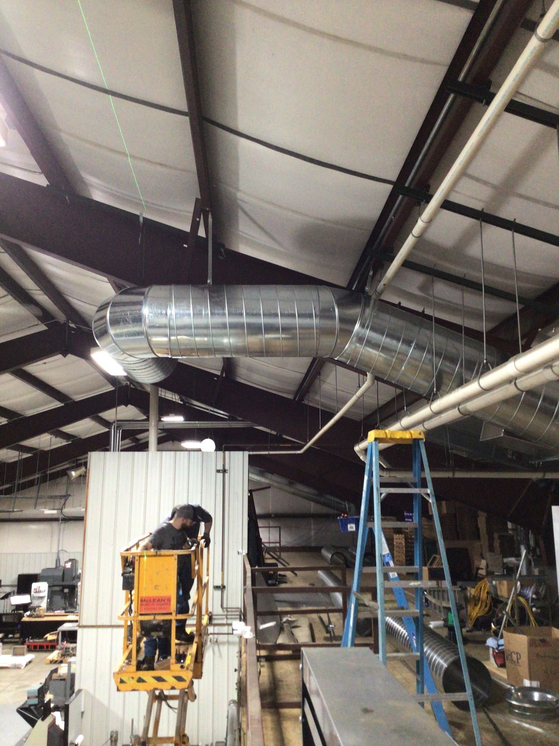 A man is sitting on a lift working on a ventilation system in a building.