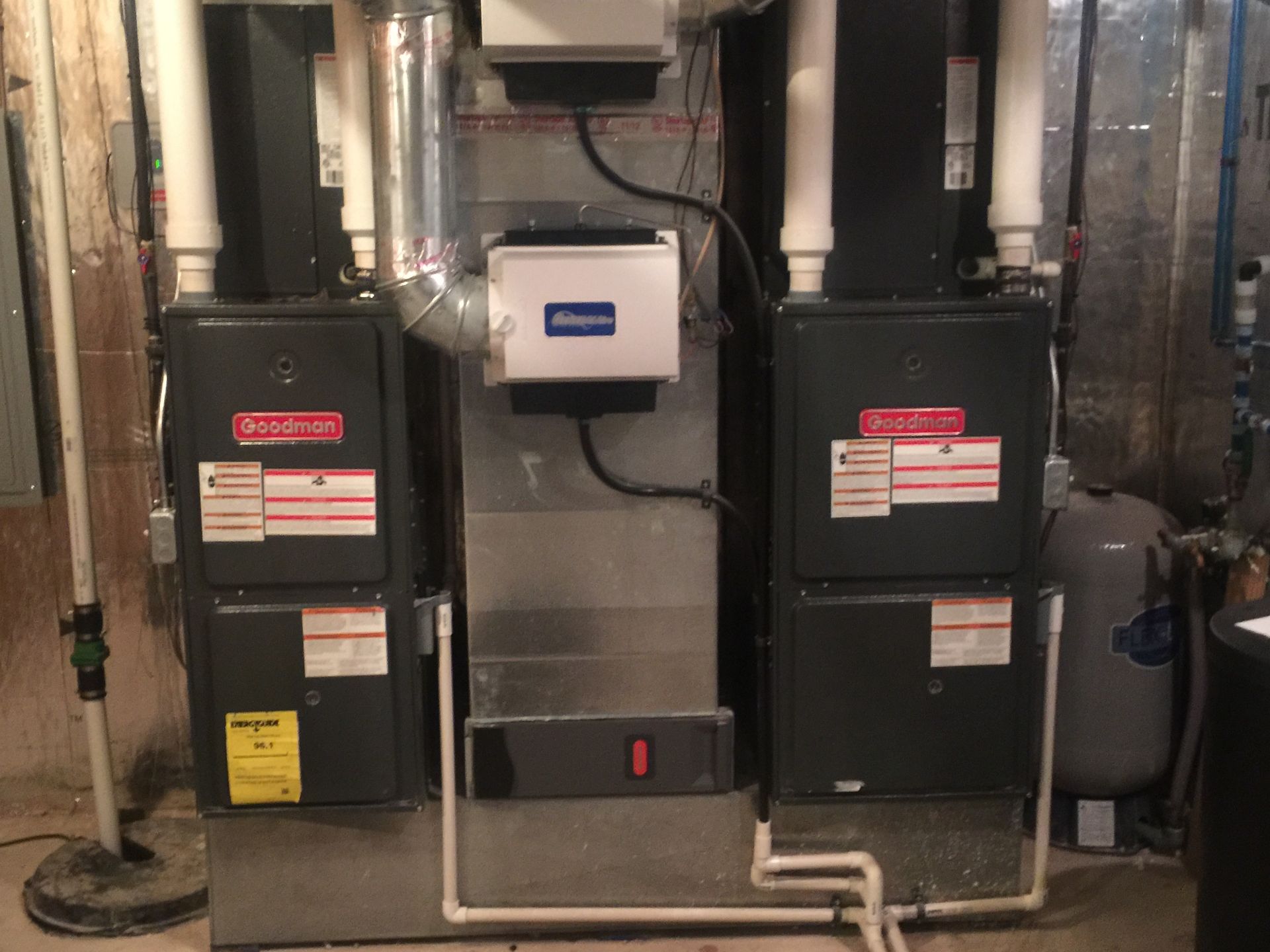 Two air conditioners are sitting next to each other in a basement.