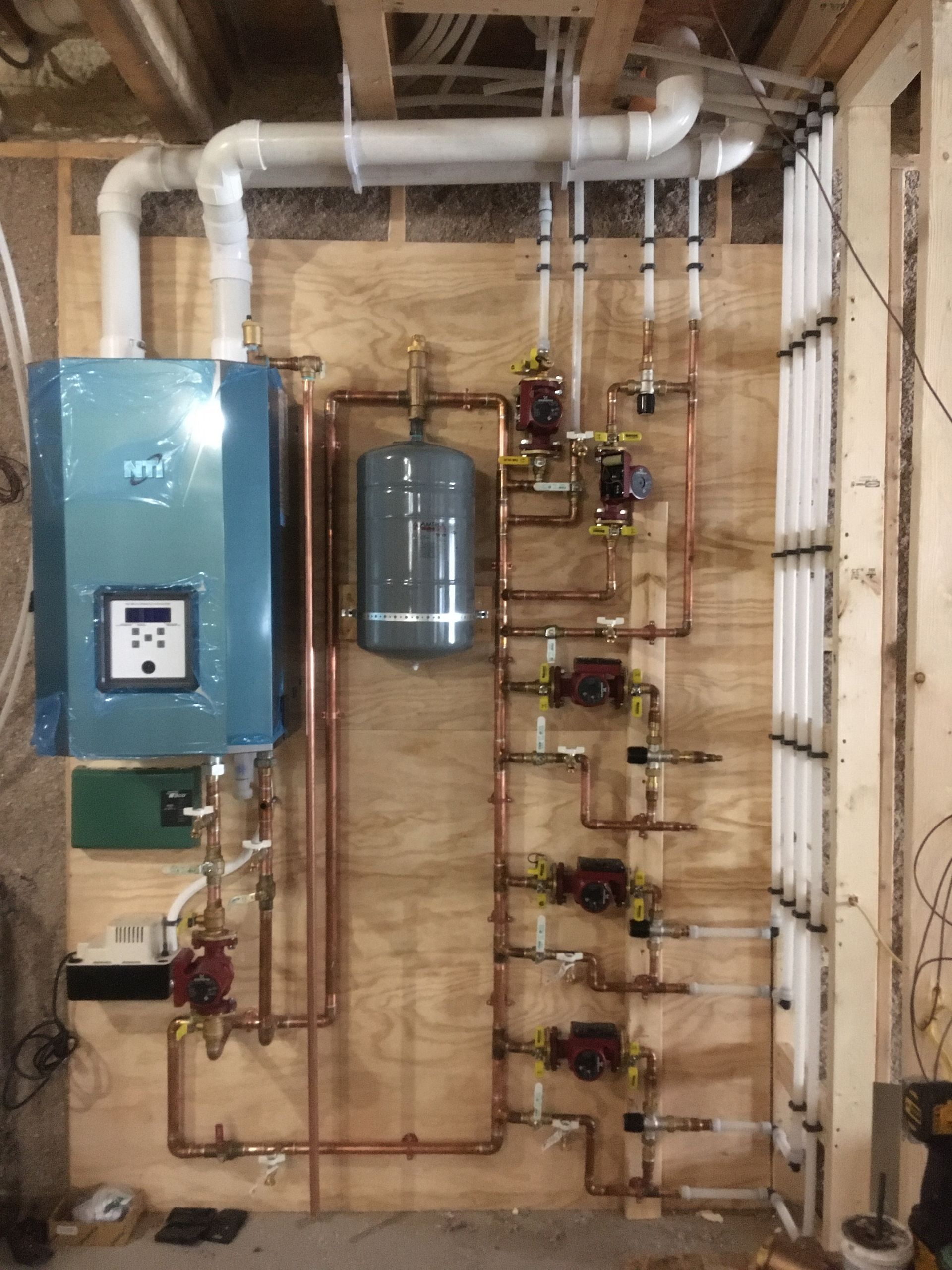 A boiler is sitting on a wall next to a bunch of pipes.