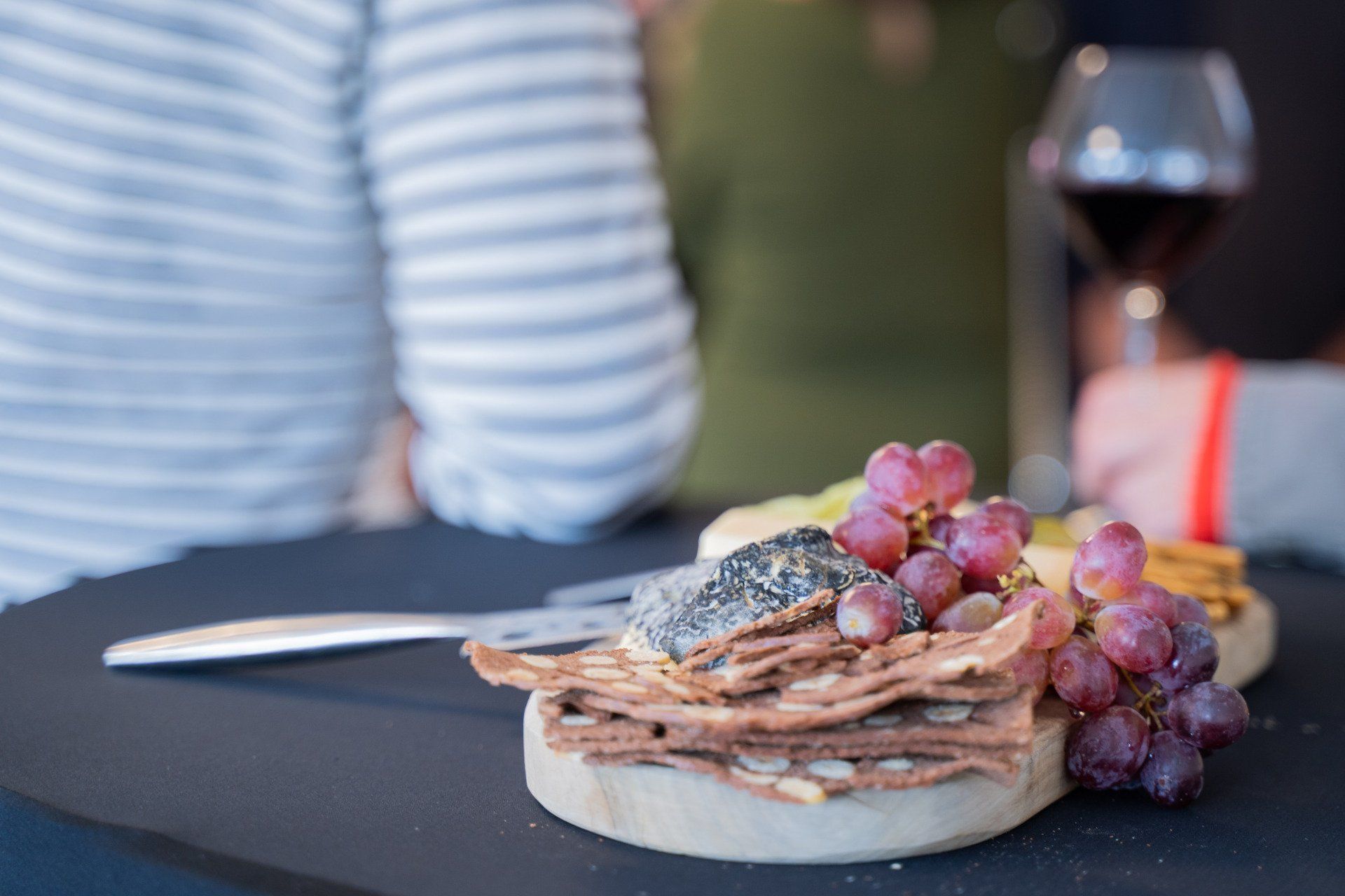 Een bord met eten, druiven en crackers op tafel, naast een glas wijn.