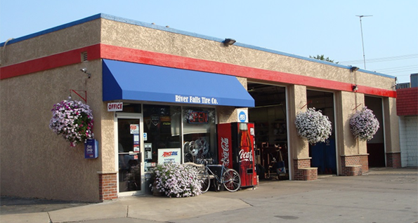 Auto repair shop exterior with blue awning, red trim, and hanging flower baskets.
