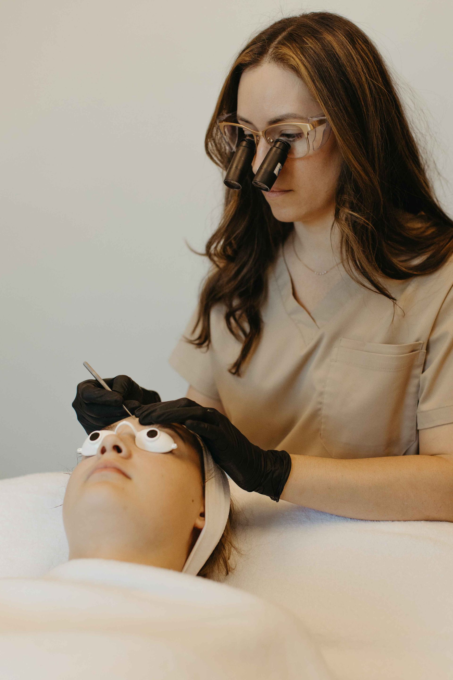 Woman wearing loupes, performing a facial procedure on a client.