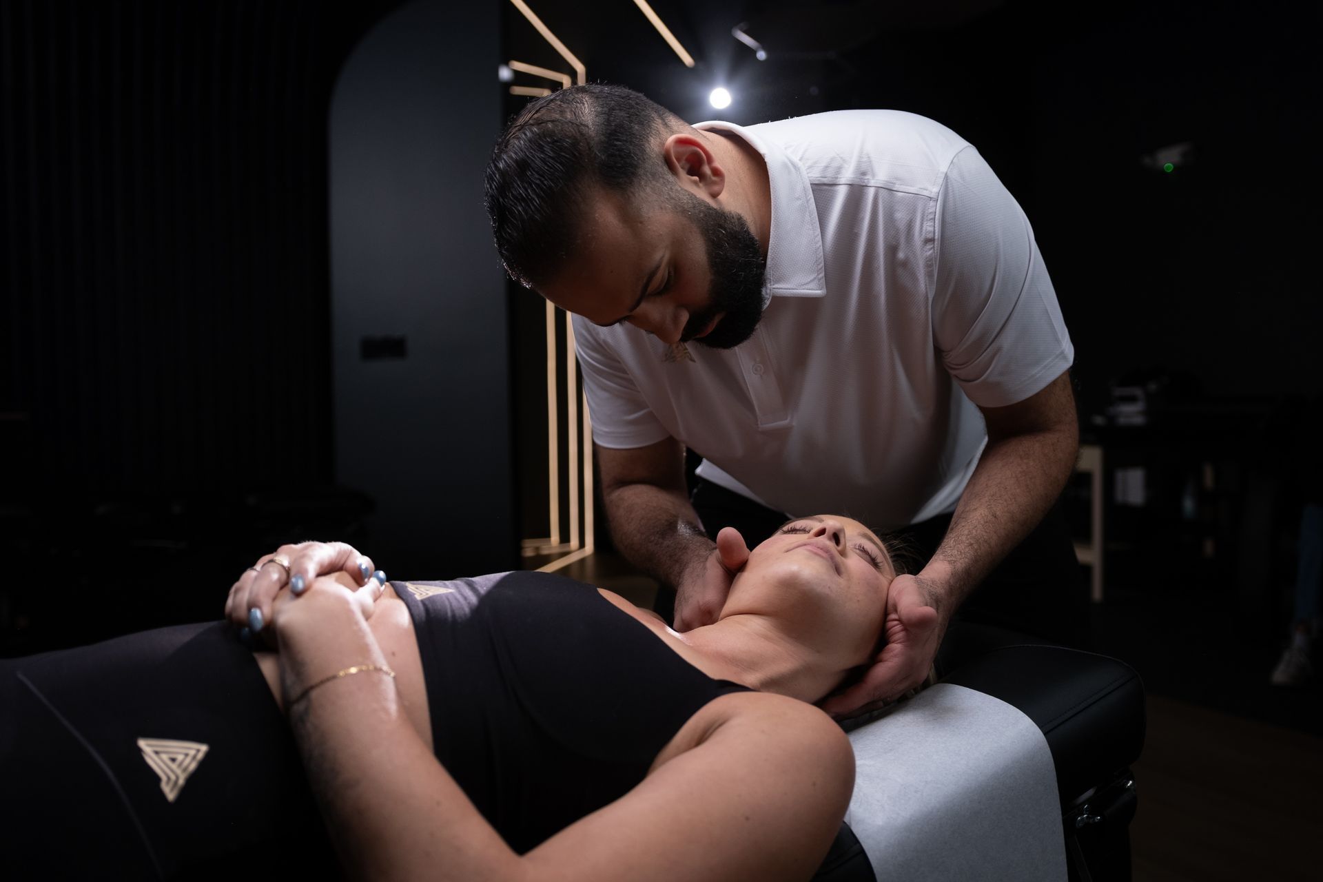 Chiropractor adjusting a patient's neck in a dark room. Patient lies on a table.