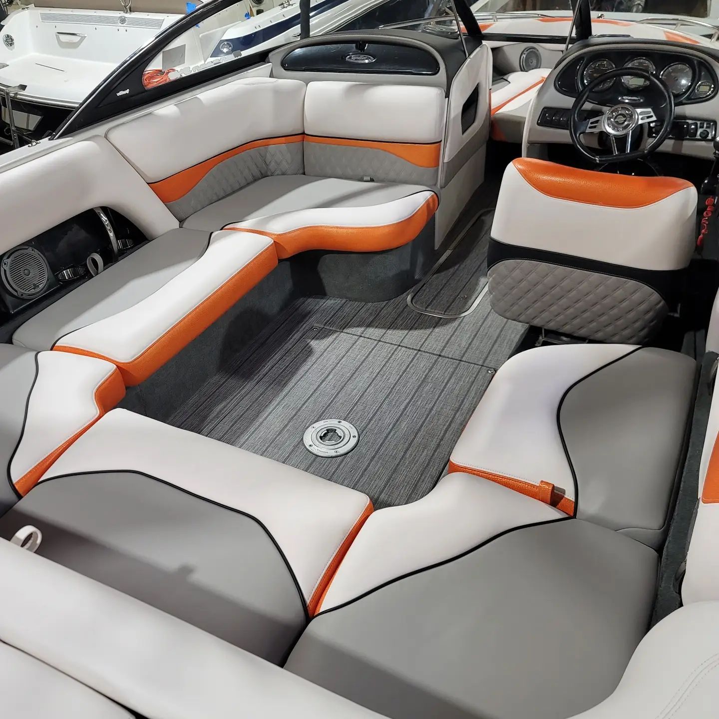 Boat interior with gray, white, and orange seating. Steering wheel visible.